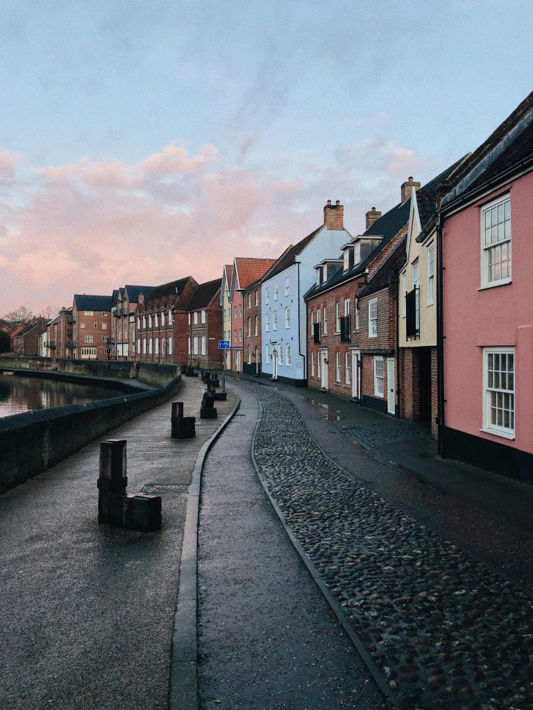 Beautiful cobblestone street in Norwich, England, showcasing colorful historic homes at dusk.